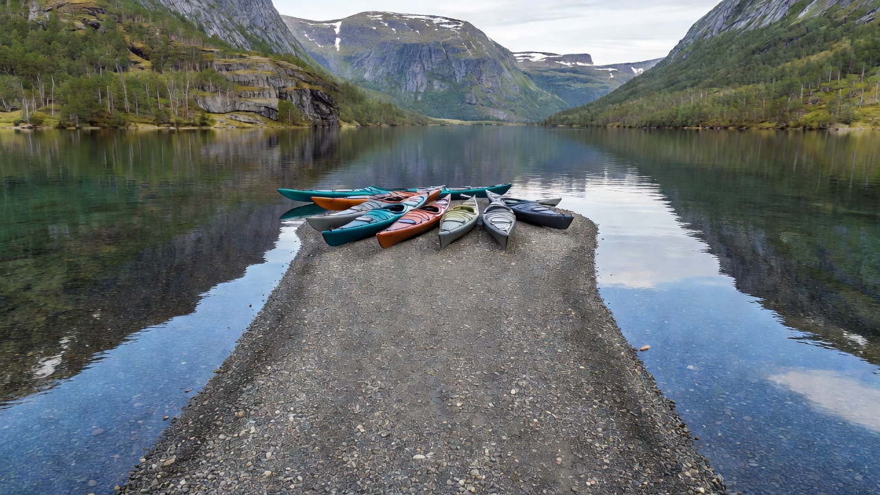Touring kayaks resting on a smooth gravel spit beside a clear Norwegian mountain lake